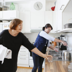 Alina omahoitaja auttaa vanhempaa naista tiskaamaan juomalasit. Hoivapalvelut vahvistavat asiakkaidensa arjessa jaksamista.