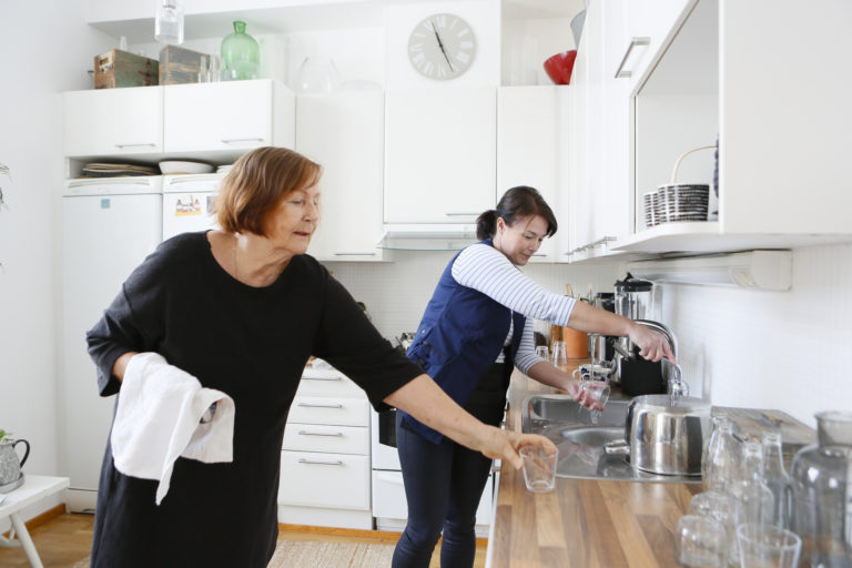 Alina omahoitaja auttaa vanhempaa naista tiskaamaan juomalasit. Hoivapalvelut vahvistavat asiakkaidensa arjessa jaksamista.